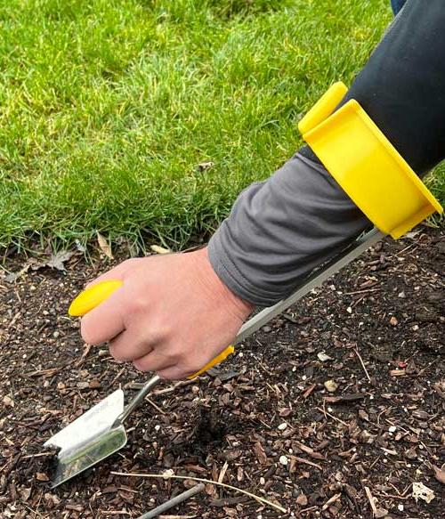 a person using a hand weeder tool that wraps around the forearm to assist